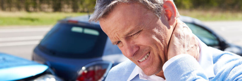 man hold his neck in pain with wrecked car behind him