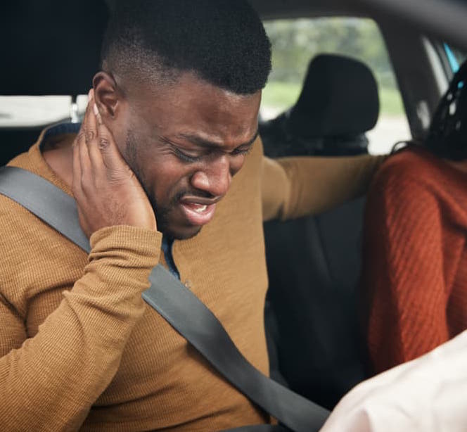 man in grimacing in pain while holding neck after car accident caused airbag deployment