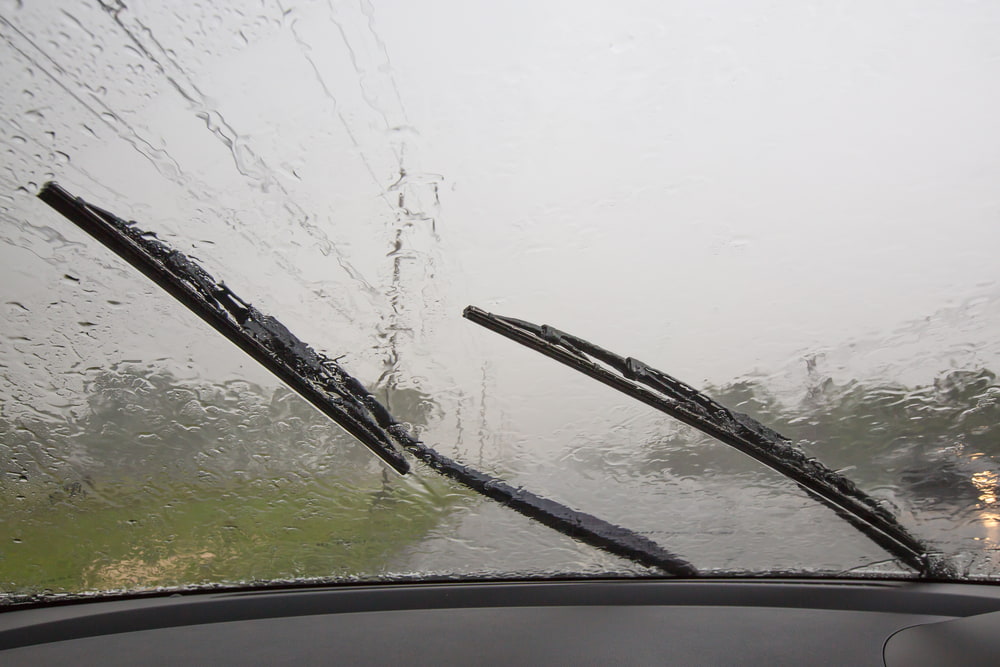 close up shot of car windshield wipers in use during rainy weather