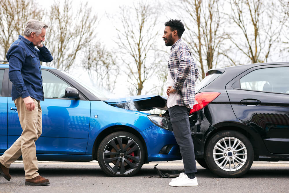 Both old and young male drivers get out of the cars and inspect the damage after a traffic accident