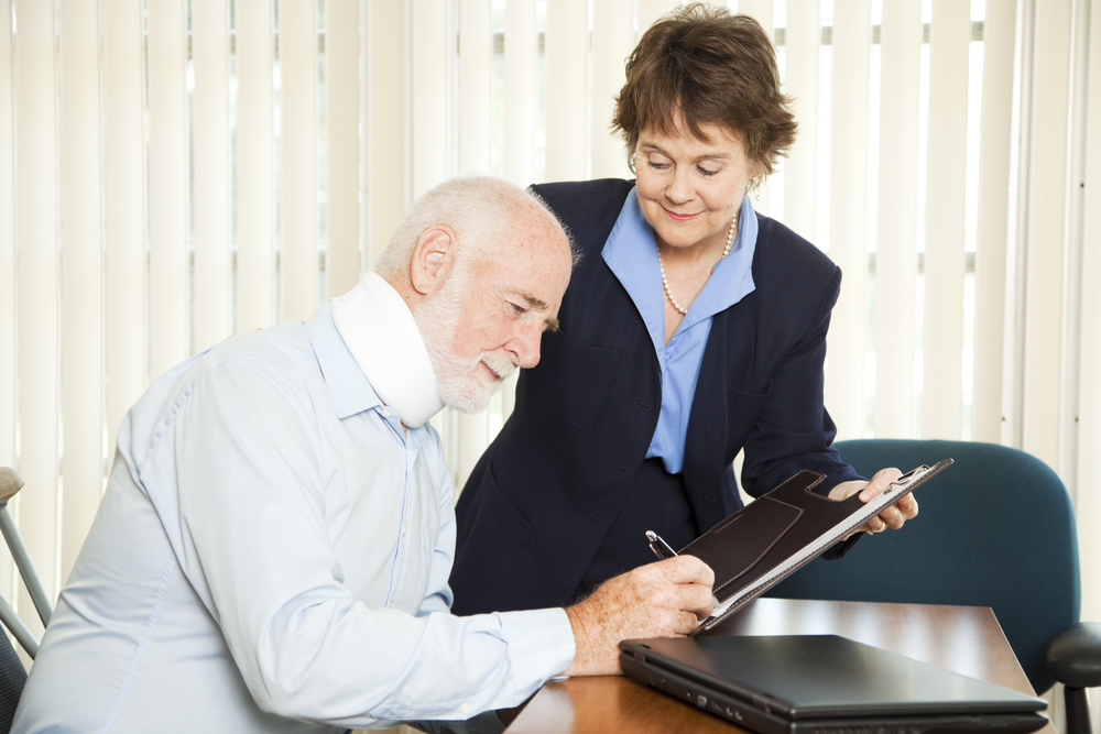 injured man sitting down signing a clipboard while a smiling lawyer holds it for him
