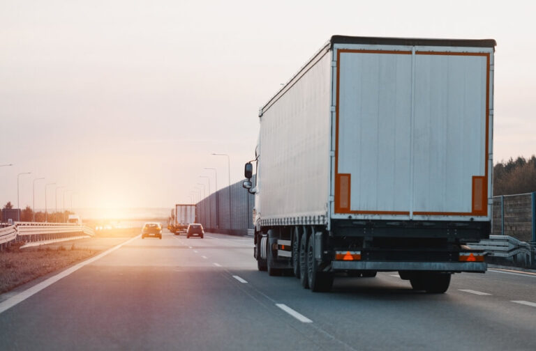 Modern white semi-trailer trucks on the highway driving in the right lane. Commercial vehicle for shipping and post delivery.