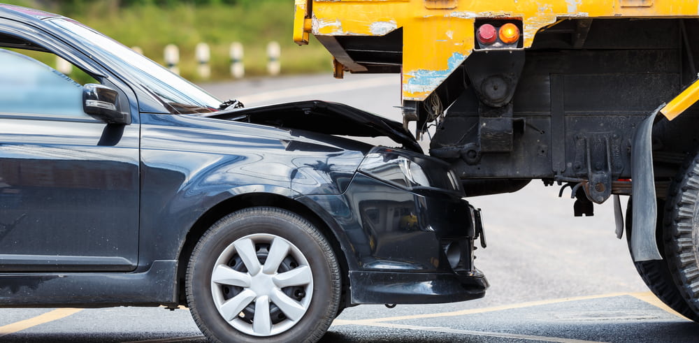 dark colored car rear ended yellow truck on road