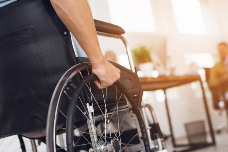 A disabled man is sitting in a wheelchair. He holds his hands on the wheel.