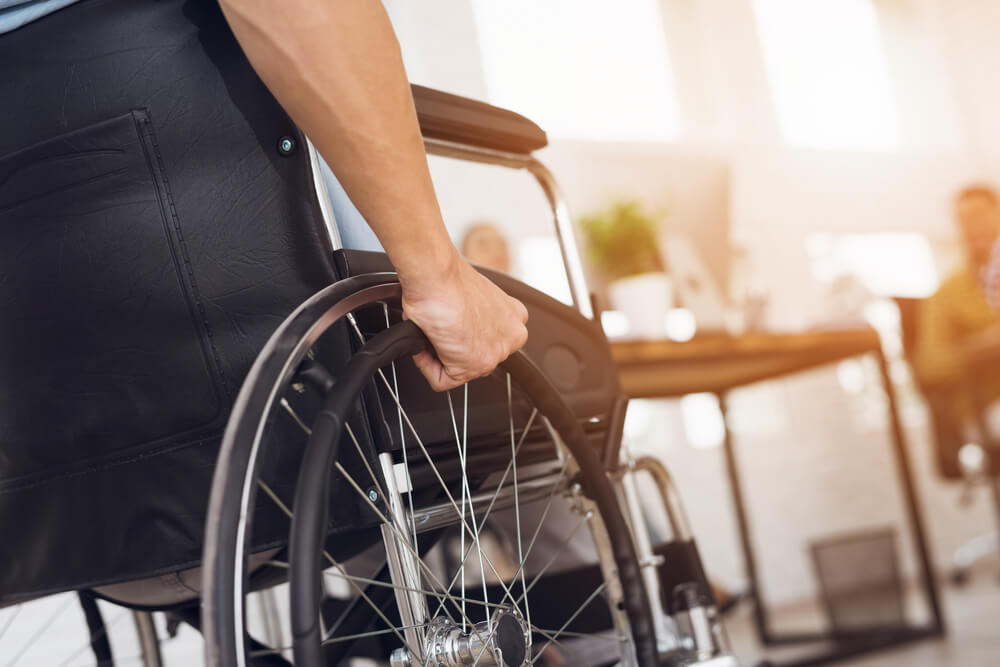 A disabled man is sitting in a wheelchair. He holds his hands on the wheel.
