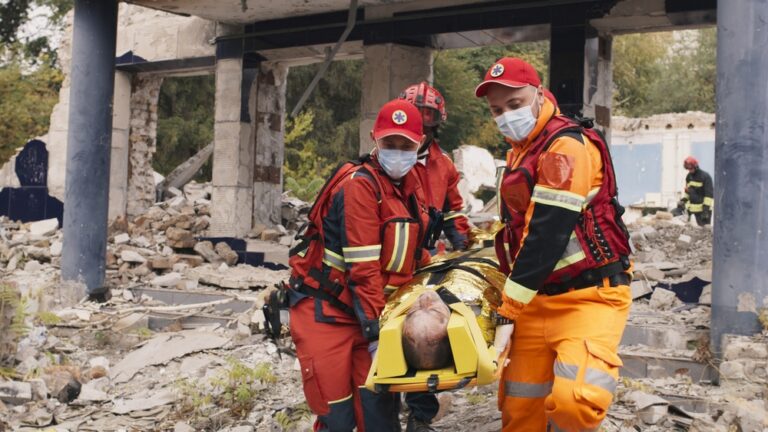 collaped building in the background, and 2 rescuers saving an injured person