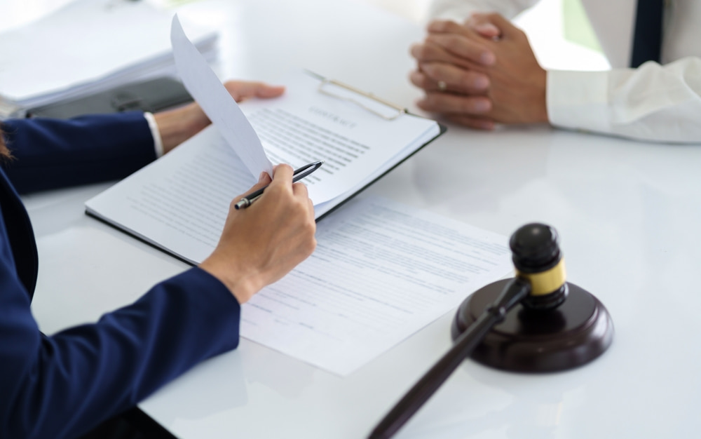 close up of two men dressed in business attire sitting across a white table with papers on a clipboard and judge's gavel next to it