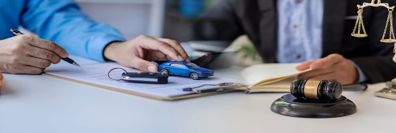 Car insurance broker holding model car, discussing options with Car Accident Lawyer.