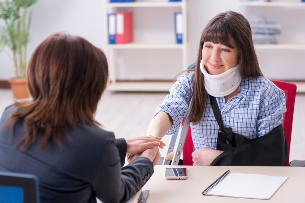 woman wearing neck brace shaking the hand of a woman attorney sitting across the desk