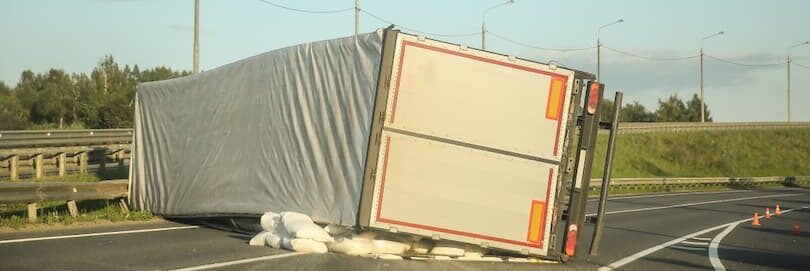 Overturned delivery truck on a highway with scattered cargo.