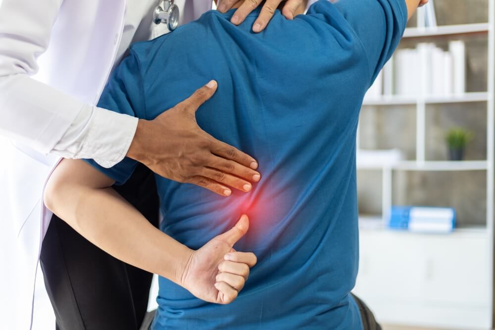 Doctor is diagnosing a patient's back pain in a hospital examination room.