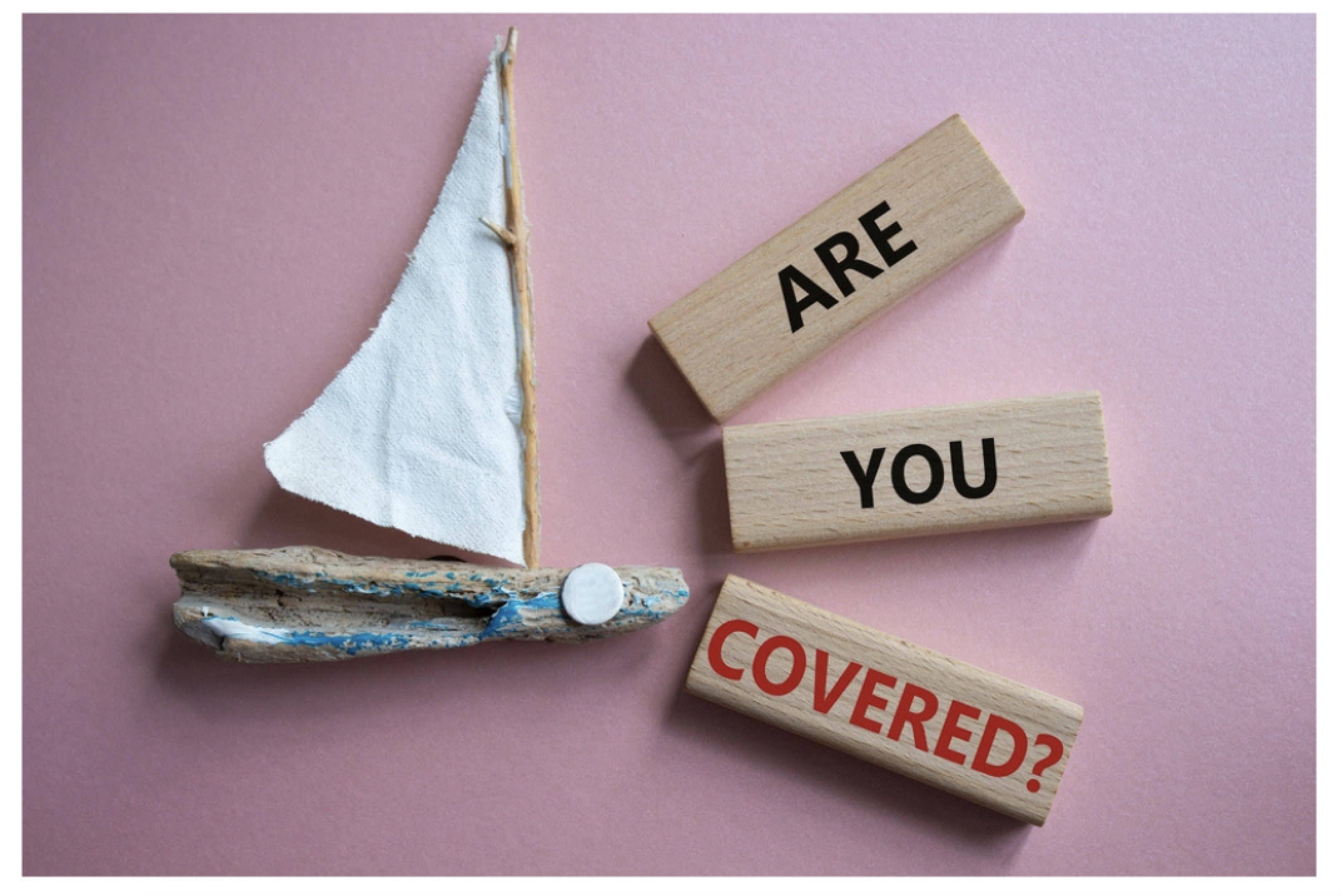 boat accident concept with wooden sailboat pictured next to blocks spelling out ARE YOU COVERED