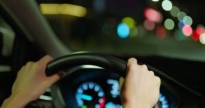 person driving with two hands gripped on the wheel at night