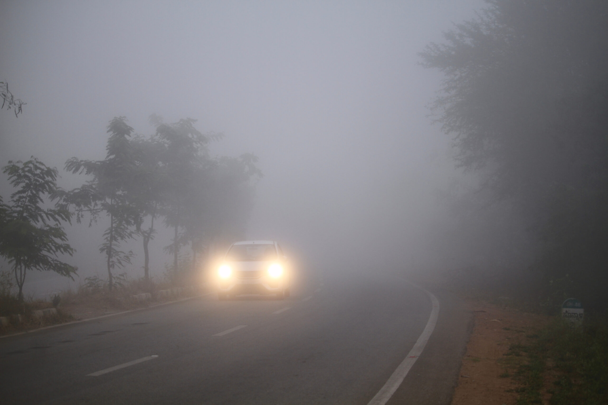 front end view of car driving through thick fog with headlights on