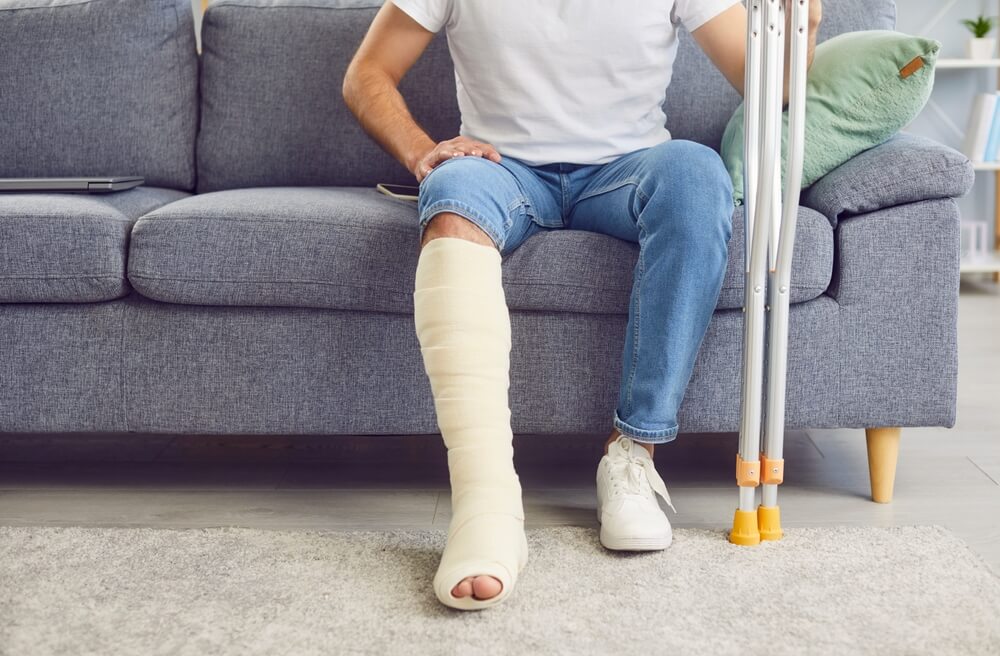 Man with leg injury from Huntsville car accident sitting on couch with crutches, illustrating personal injury recovery.
