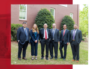 six attorneys in suits standing on the side lawn of a brick office building
