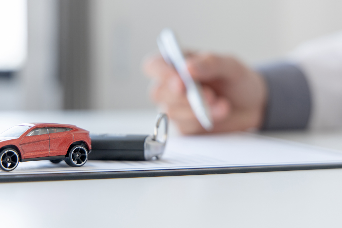 red model car with a set of keys on a table with a person's hand holding a pen and paperwork